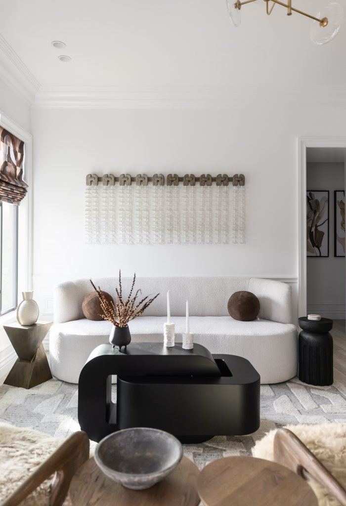 Modern living room featuring a white curved sofa, black coffee table, decorative vases, neutral cushions, and wall art—Living with Lolo.