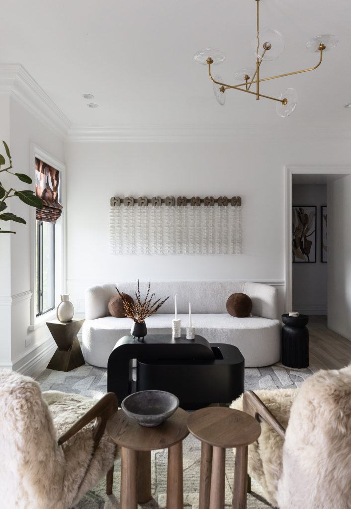 Modern living room with a white sofa, two tan fur chairs, black coffee table, abstract wall art, and a gold chandelier — Living with Lolo.