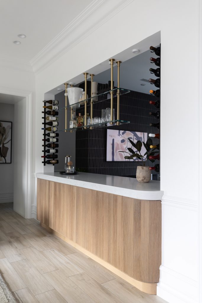 Modern home bar with wooden cabinets, open glass shelves, wine racks on both sides, and a potted plant on a tiled counter— Living with Lolo.