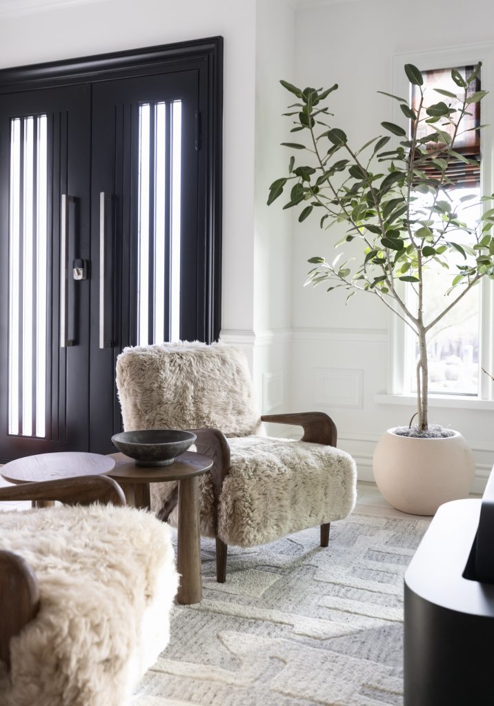 Two fur-covered armchairs, a small round table, a potted plant, and double black doors with vertical glass panels. — Living with Lolo.
