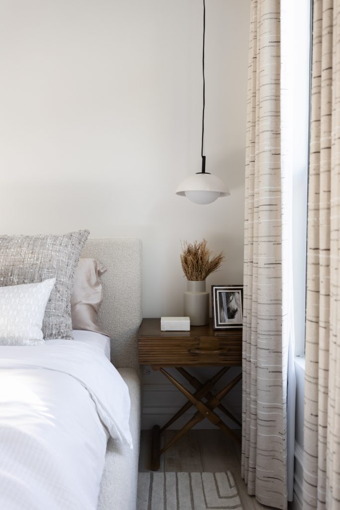 A modern bedroom features a neatly made bed, a wooden nightstand with decor, and a pendant light above— Living with Lolo.