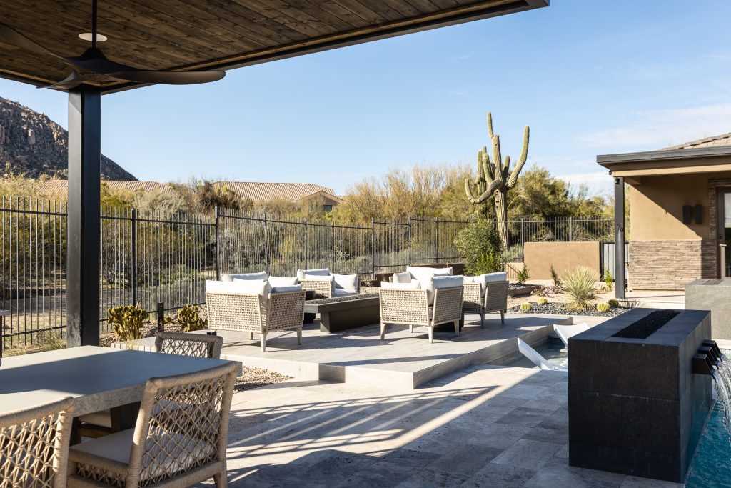 Modern outdoor patio featuring wicker furniture, a dining table, desert landscaping, and a metal fence—Living with Lolo.