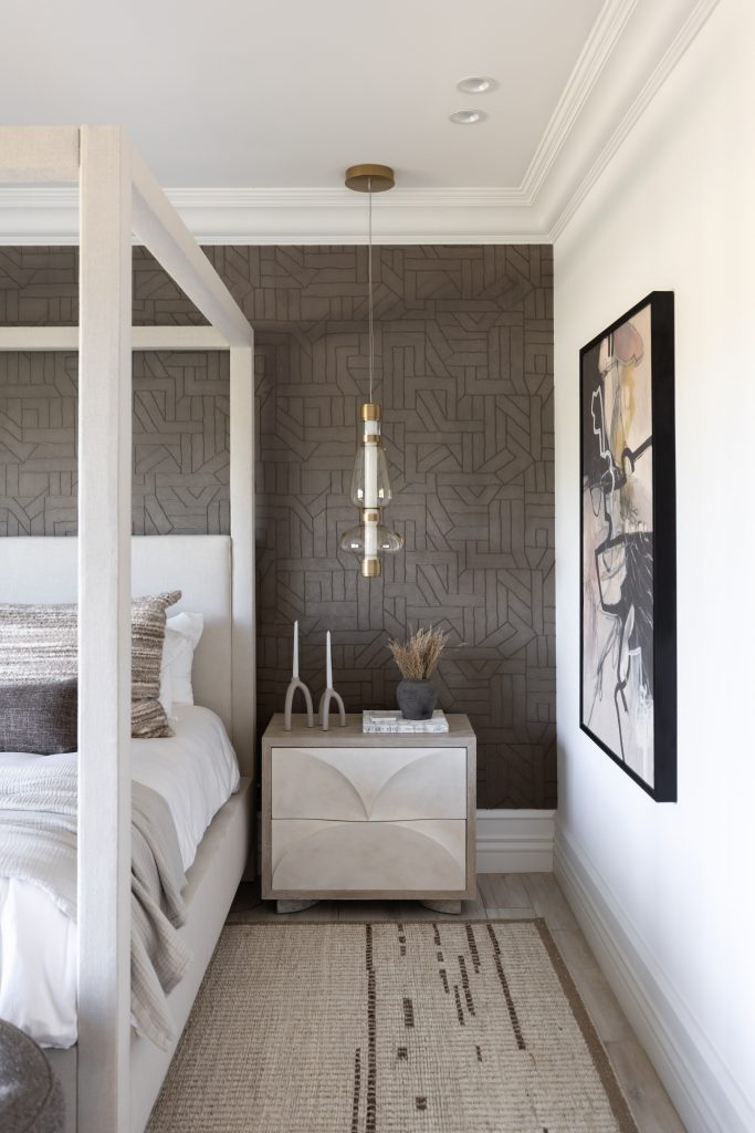 Modern bedroom featuring a canopy bed, geometric wallpaper accent wall, hanging pendant light, abstract art, and nightstand—Living with Lolo.