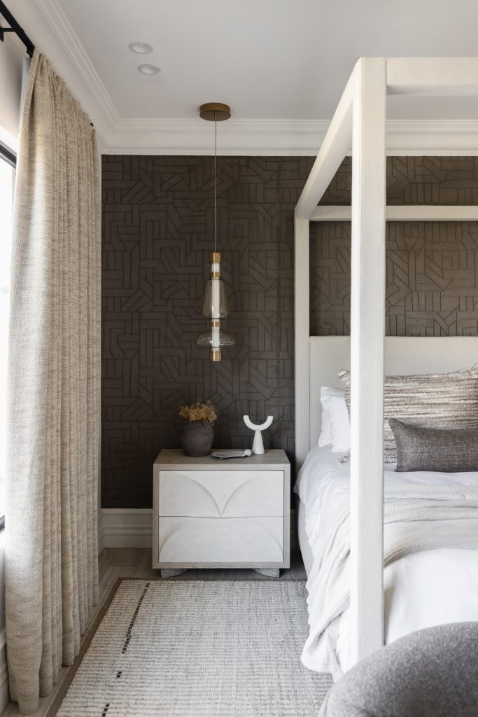 A modern bedroom with a white canopy bed, geometric accent wall, light wood nightstand, pendant light, and neutral curtains — Living with Lolo.