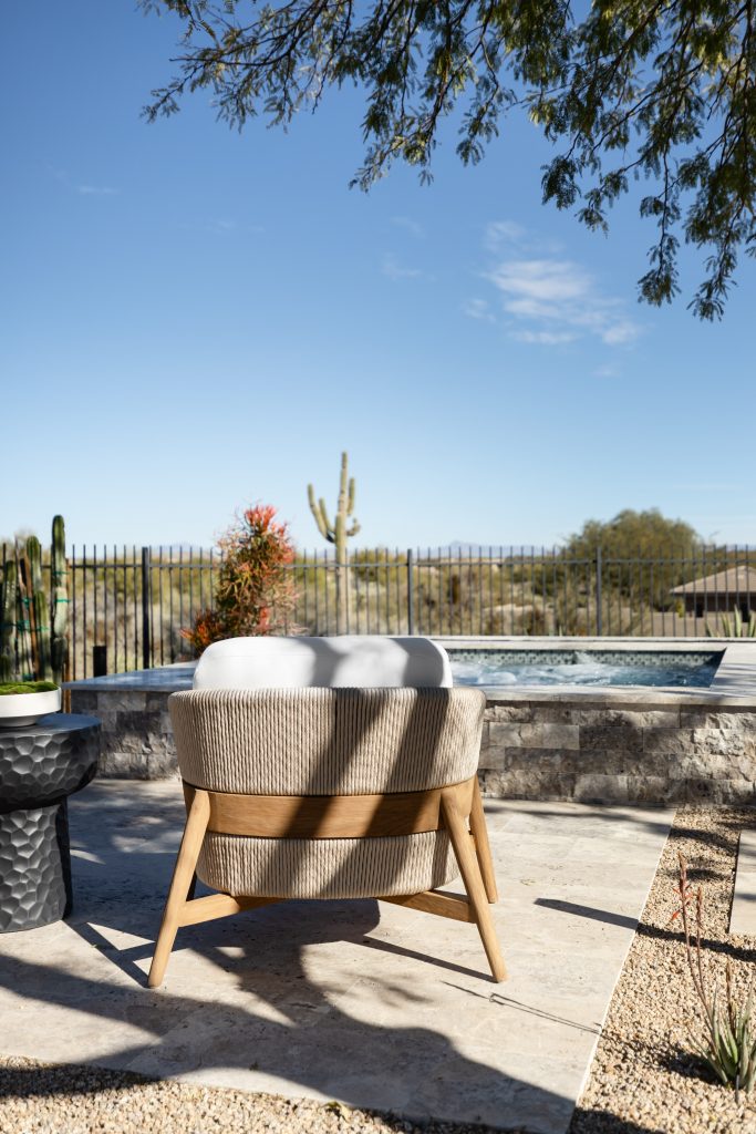 A cushioned outdoor chair faces a small pool, with desert plants and stone pavement arranged in the backyard—Living with Lolo.