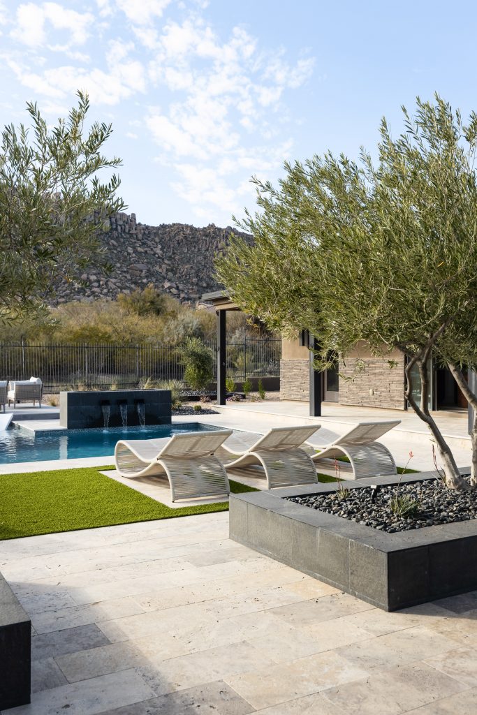 Outdoor pool area featuring sculptural lounge chairs, stone paving, and surrounding trees with rocky hills in the background—Living with Lolo.