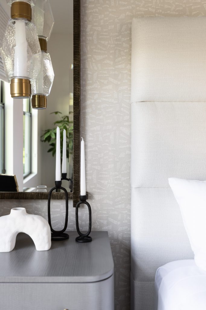 A modern bedside table displays two black candlesticks, a white abstract sculpture, and a mirror reflecting a window and lights. — Living with Lolo.