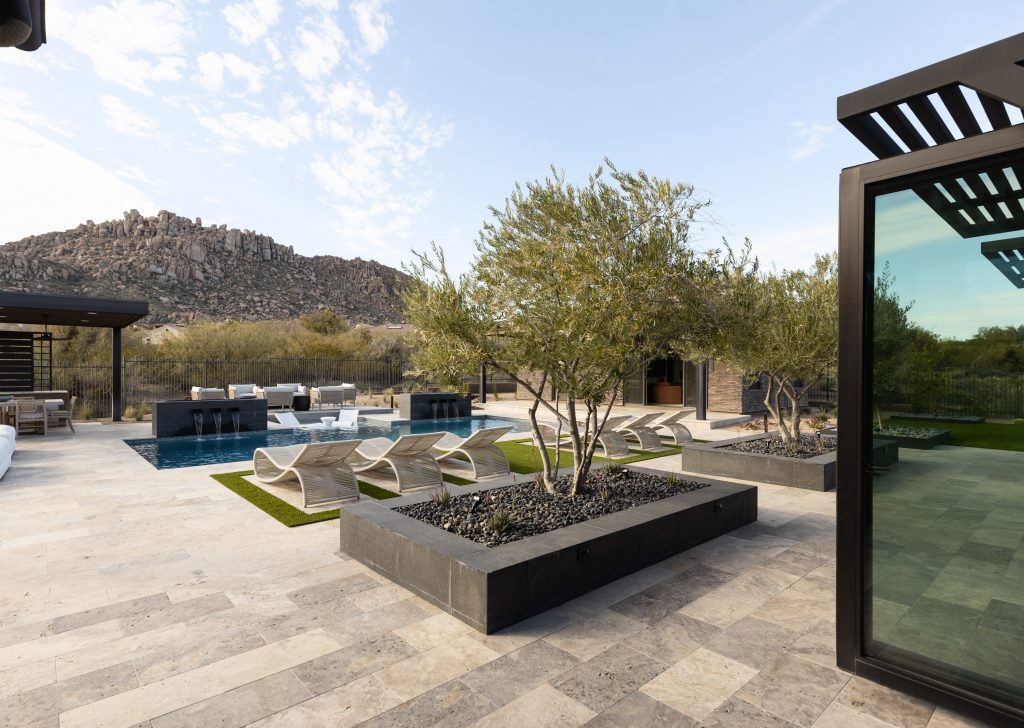 Outdoor patio with lounge chairs, a small pool, bar seating, stone tile flooring, and planter boxes—Living with Lolo.