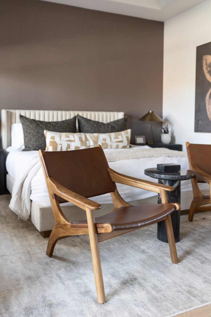 A modern bedroom features a wooden chair with a brown leather seat, a black side table, and a bed with neutral bedding. — Living with Lolo.