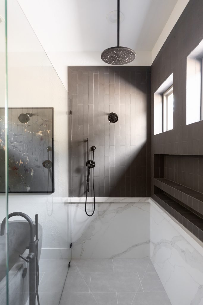A bathroom shower with dark vertical tiles, a rainfall showerhead, handheld shower, and built-in shelving by the window. — Living with Lolo.