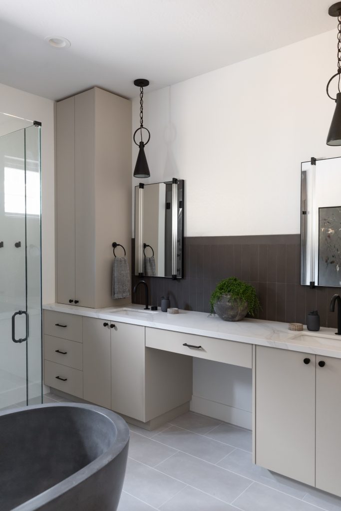 Modern bathroom with light gray cabinets, dual sinks, black fixtures, a round black tub, two mirrors, pendant lights, and a small plant—Living with Lolo.