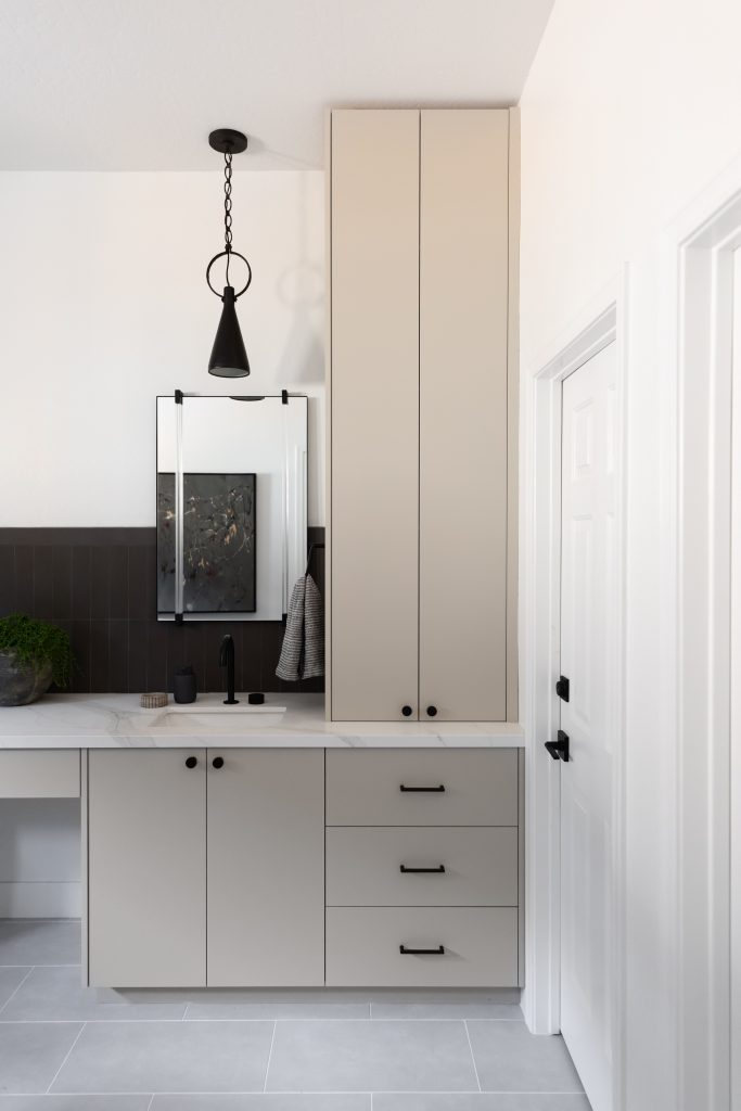 Modern bathroom featuring tall beige cabinets, a small vanity, black fixtures, wall mirror, and grey tile flooring— Living with Lolo.