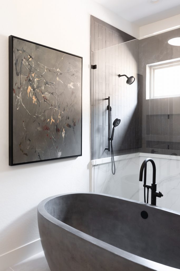 Modern bathroom with a dark freestanding bathtub, black fixtures, abstract wall art, and a glass shower with rainfall showerhead—Living with Lolo.