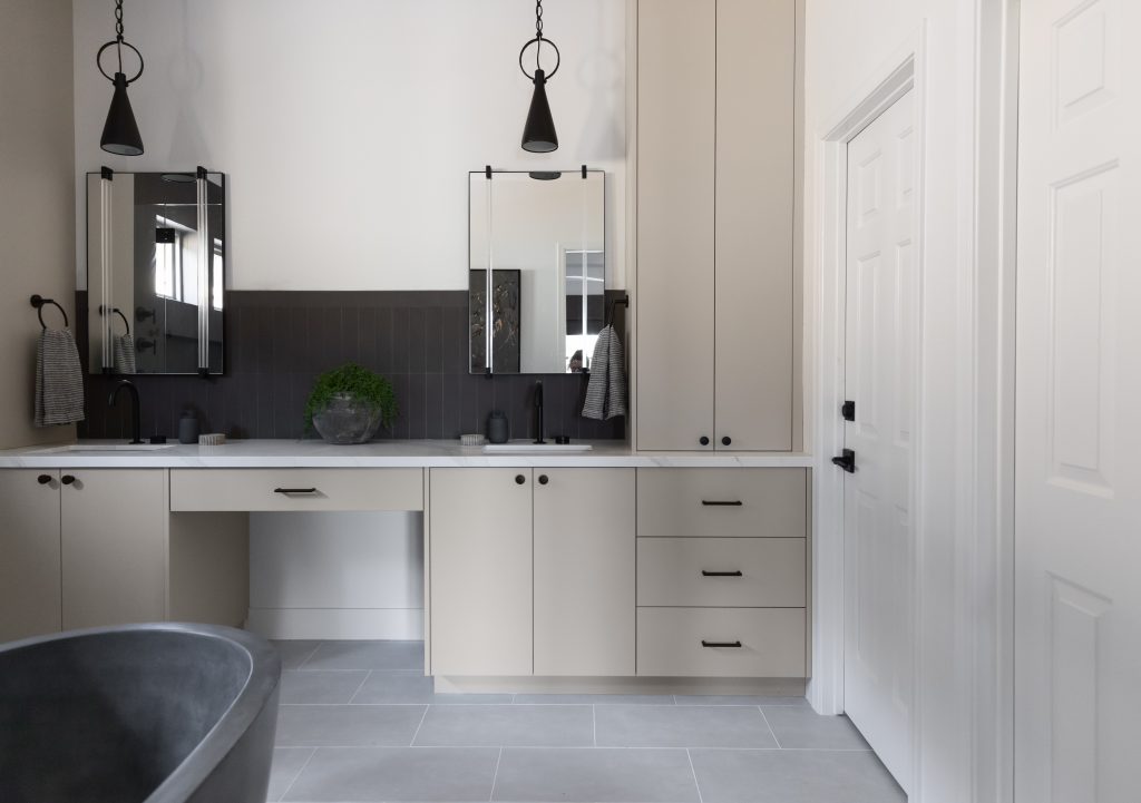 Modern bathroom with double vanity, two square mirrors, black fixtures, beige cabinets, gray tiled floor, and a partial bathtub—Living with Lolo.