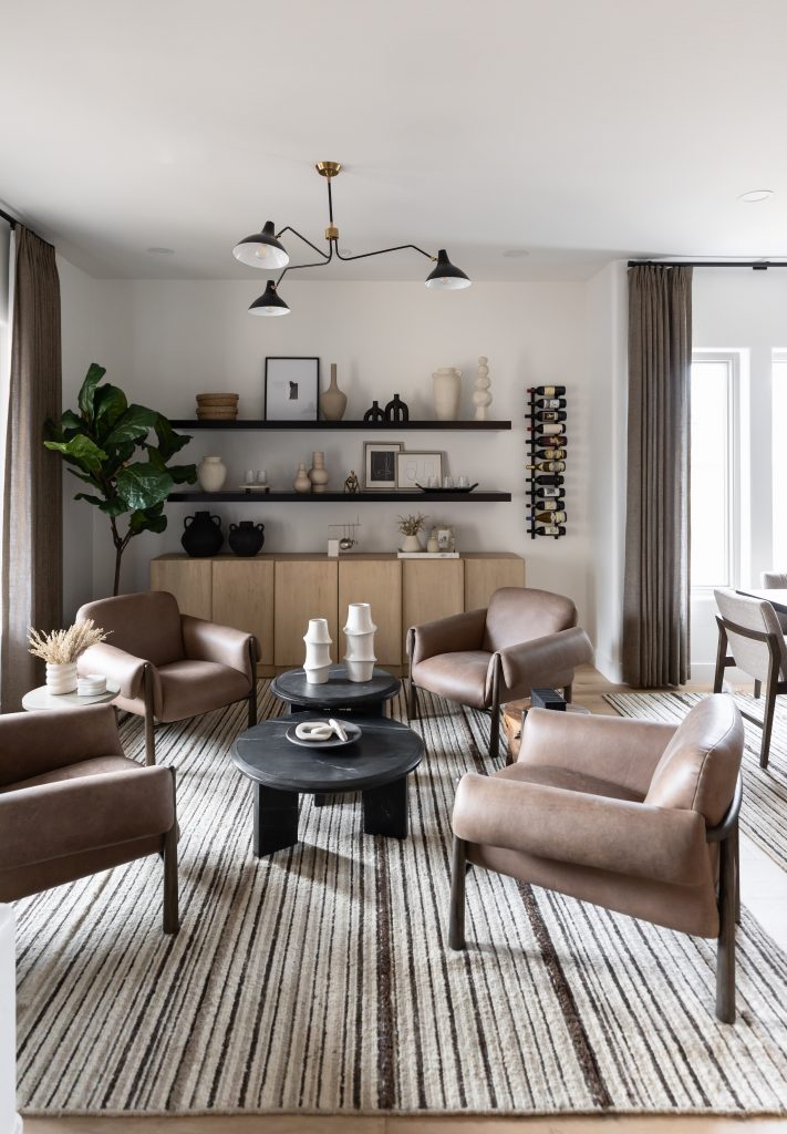 Four brown leather armchairs surround a black coffee table on a striped rug, with wall shelves and large windows with taupe curtains. — Living with Lolo.