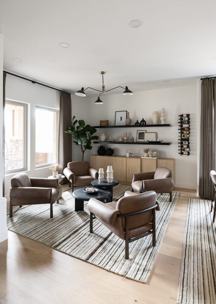 Modern living room with four brown leather chairs, striped rugs, a round black coffee table, wooden cabinets, and large windows—Living with Lolo.