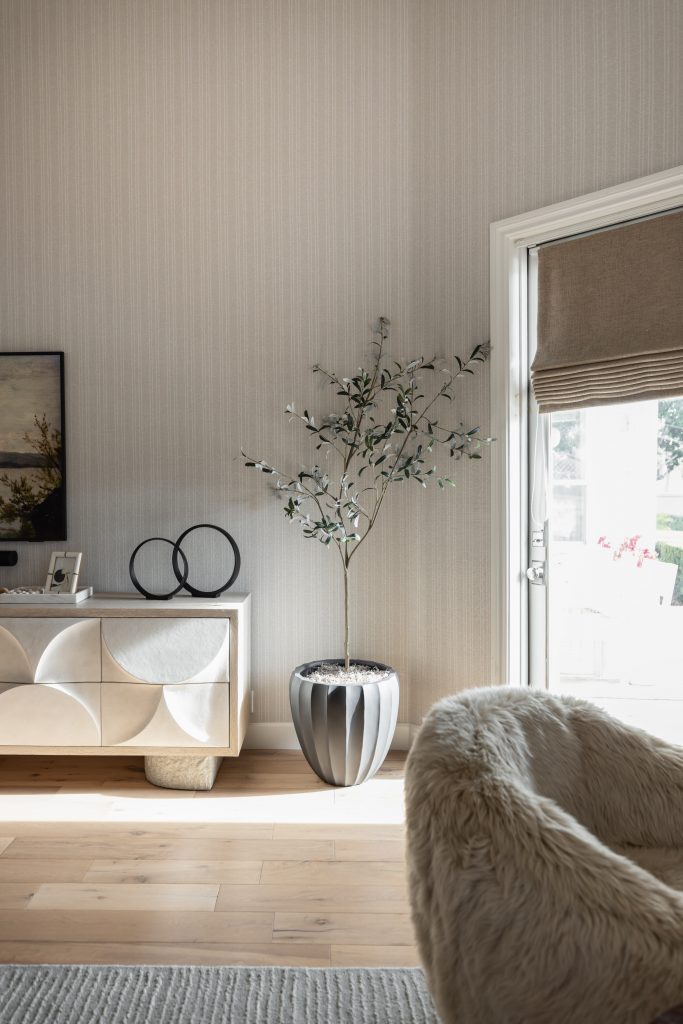 A modern living room corner with a potted plant, a light sideboard, textured armchair, wood floor, and glass door. — Living with Lolo.