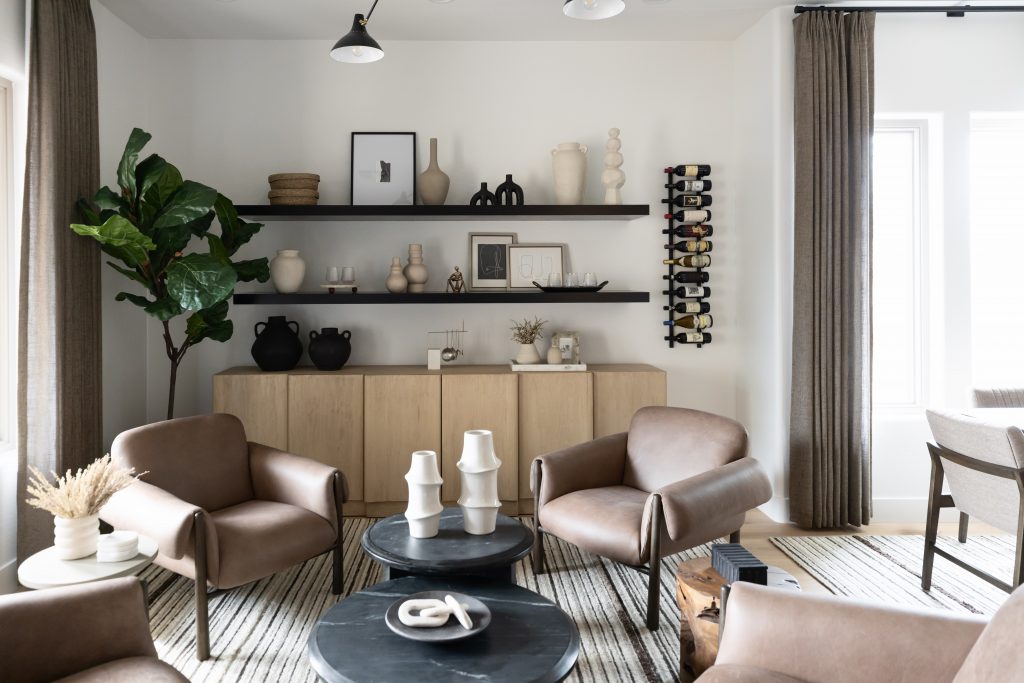 Brown leather chairs, black round tables, a large potted plant, and shelves with neutral-toned decor are visible—Living with Lolo.