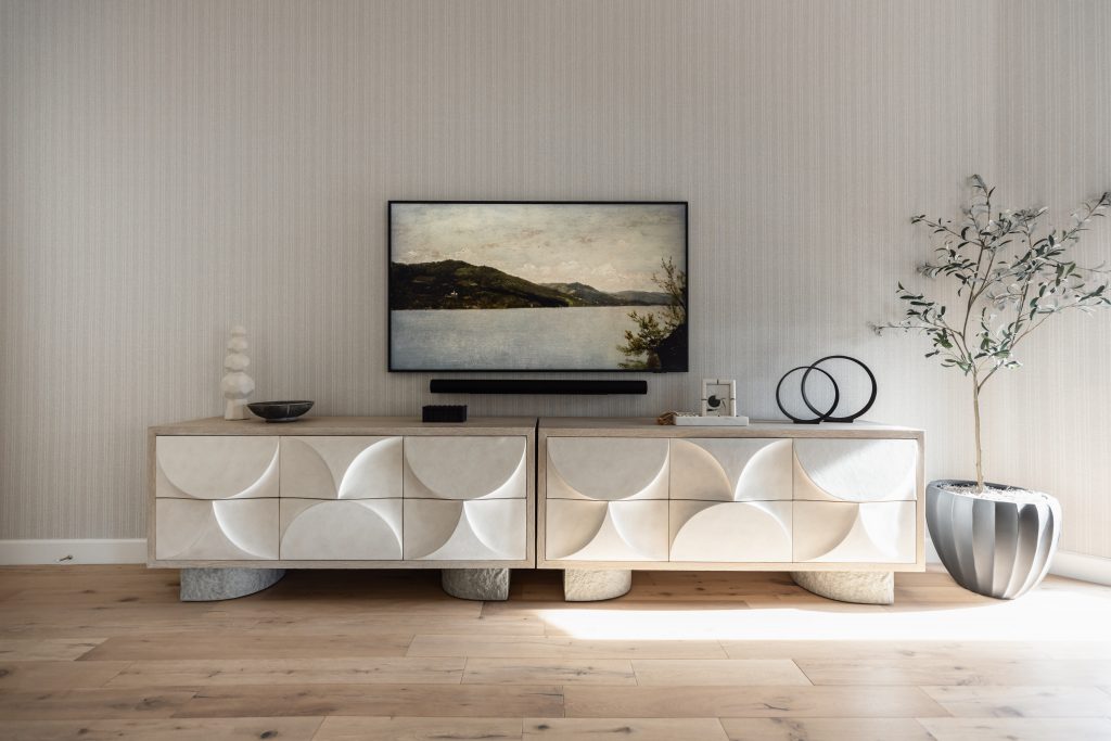 A modern living room with a geometric patterned sideboard, TV displaying a landscape, stylish decor, and a potted plant on wood flooring— Living with Lolo.