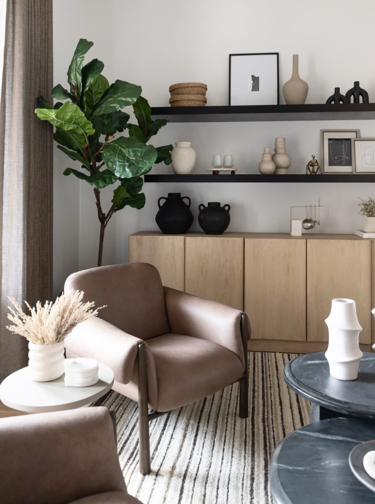 Modern living room with taupe armchairs, a striped rug, minimalist shelf decor, potted plant, and light wood furniture—Living with Lolo.