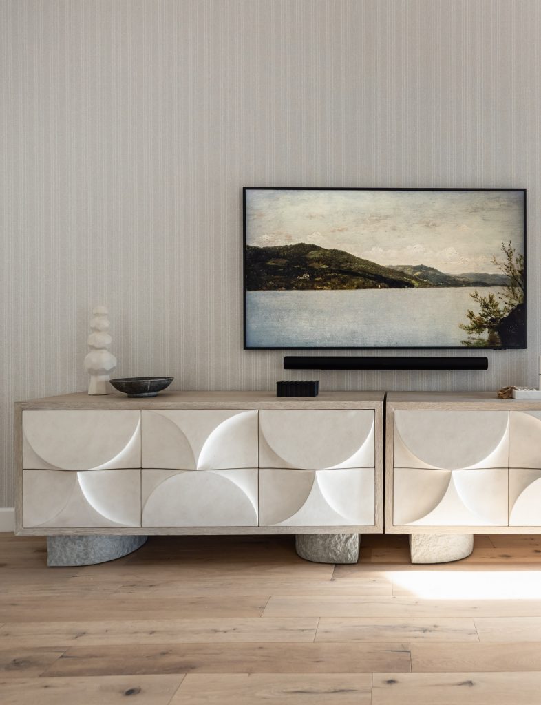 A modern sideboard with geometric patterns sits on a wooden floor, holding decor objects and a flat-screen TV with art—Living with Lolo.