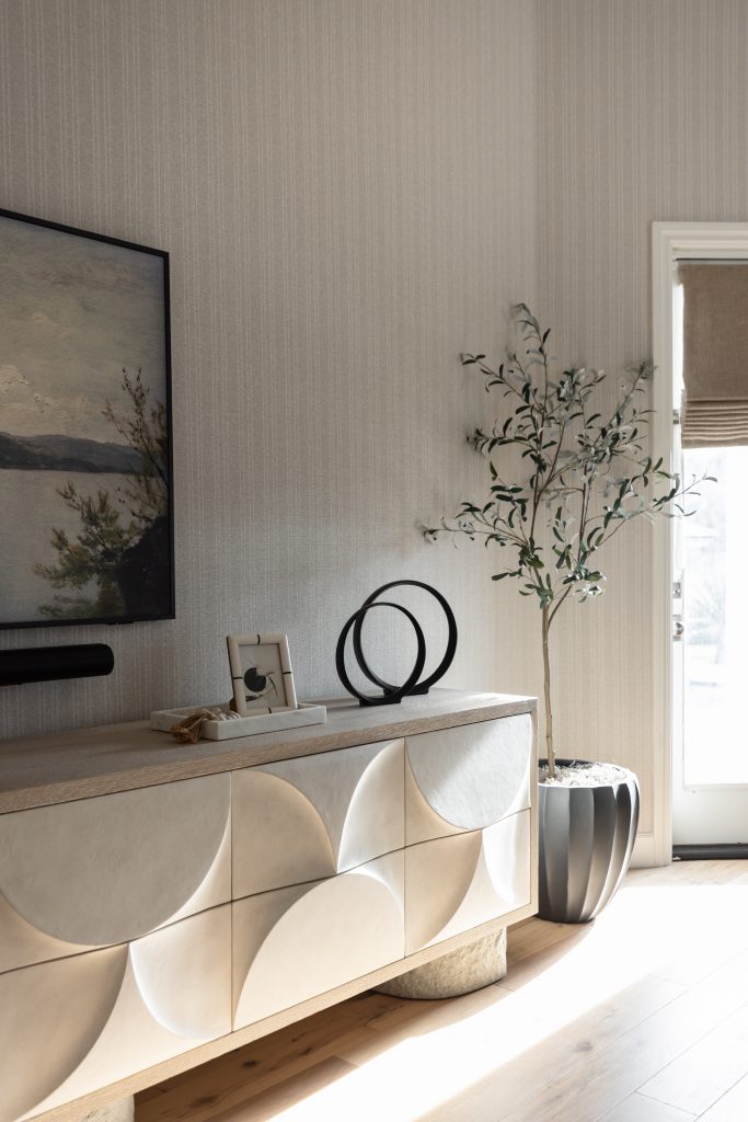 A modern sideboard with geometric patterns displays black circular sculptures, a photo frame, and decor; a potted plant stands nearby—Living with Lolo.