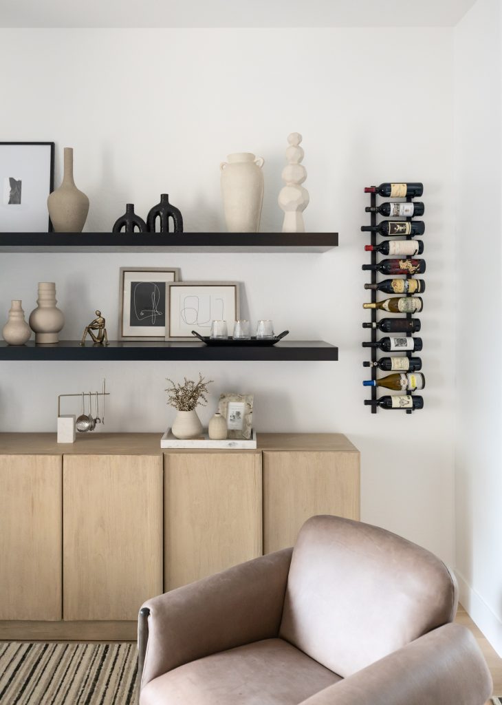 Beige armchair, wooden cabinets, black floating shelves with decor, and wall-mounted wine rack with bottles — Living with Lolo.