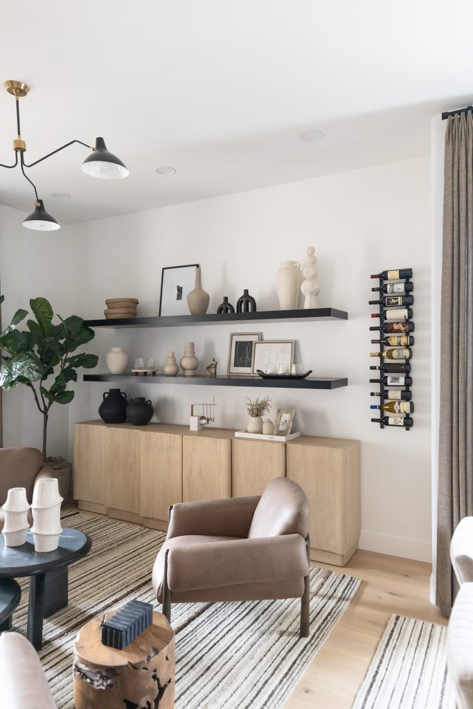 Modern living room with tan armchairs, a striped rug, open shelving, wall-mounted wine rack, and a large potted plant—Living with Lolo.