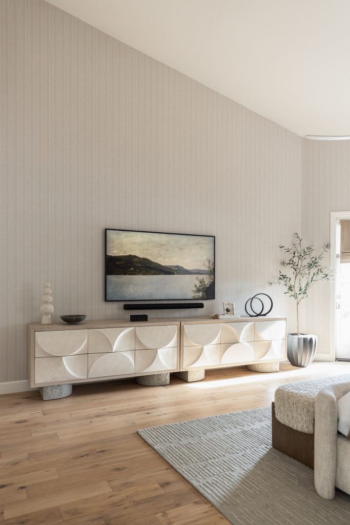 A modern living room features a geometric-patterned sideboard, landscape painting, TV, potted plant, and light wood floor. — Living with Lolo.