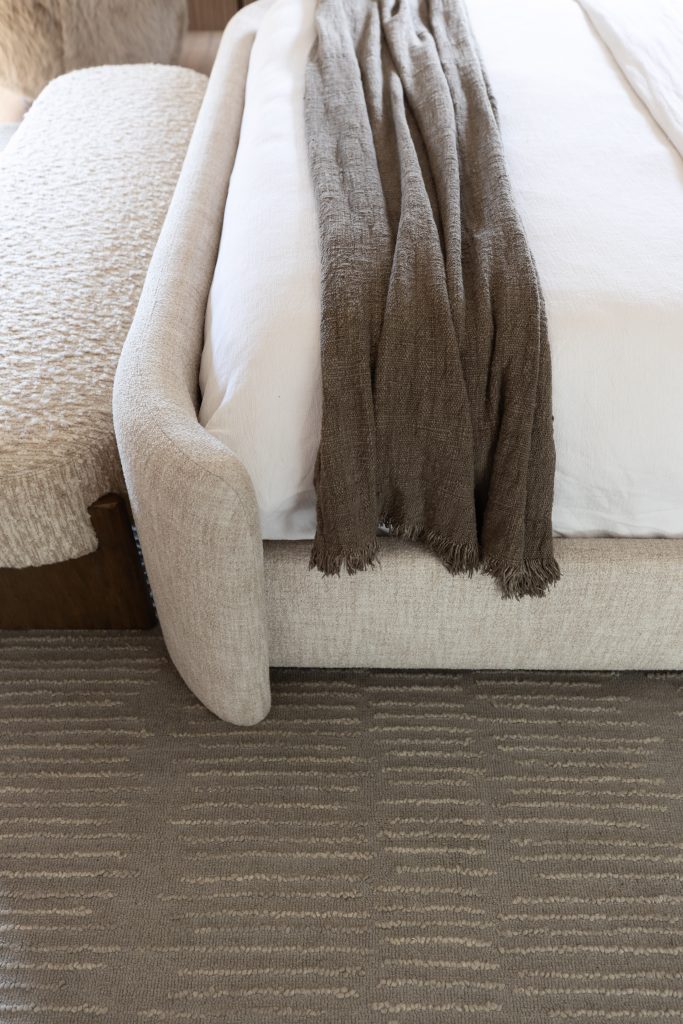 A close-up of a neatly made bed with a beige upholstered frame, a textured bench at the foot, and a brown throw on white bedding. — Living with Lolo.