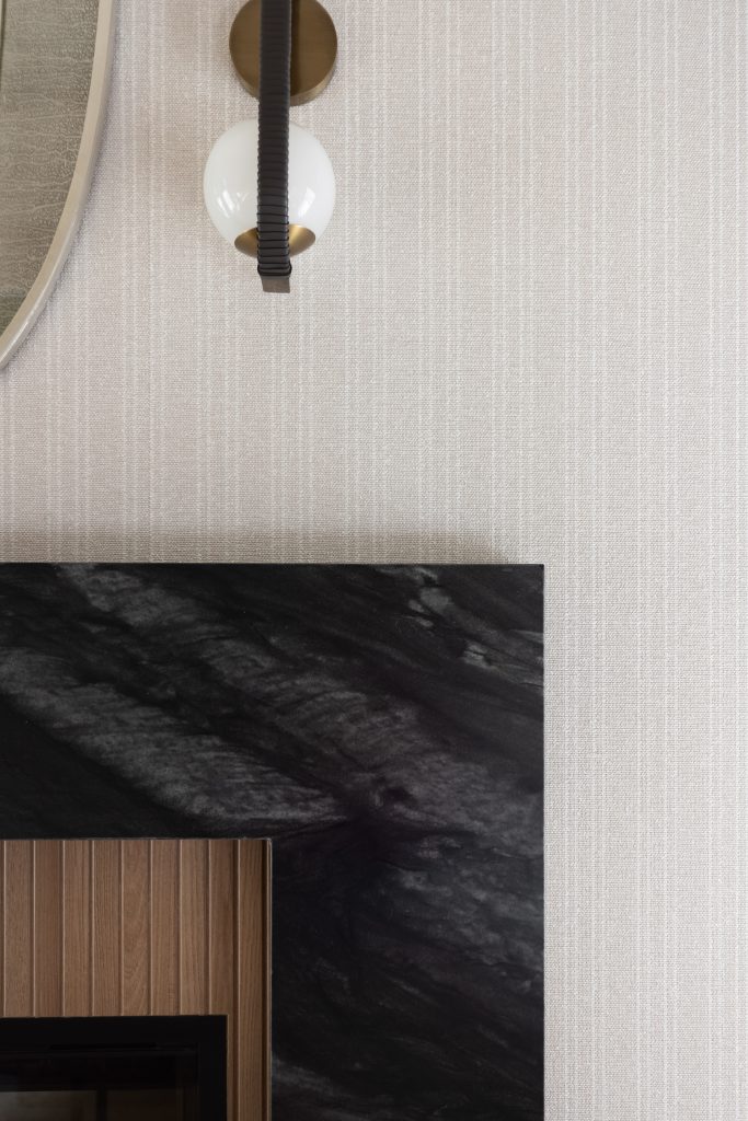 A round wall sconce with a white globe and black accent is mounted above a fireplace with black marble and wood surround—Living with Lolo.