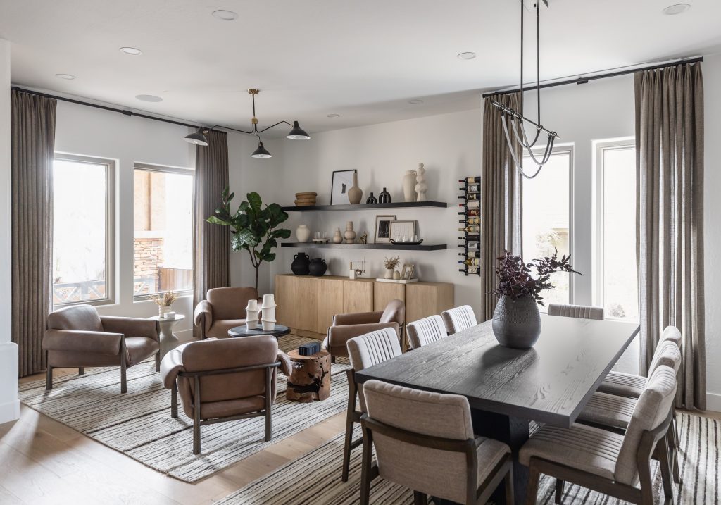 Neutral-toned living and dining area with leather chairs, a dark table, open shelves, an indoor plant, and large windows with gray curtains—Living with Lolo.