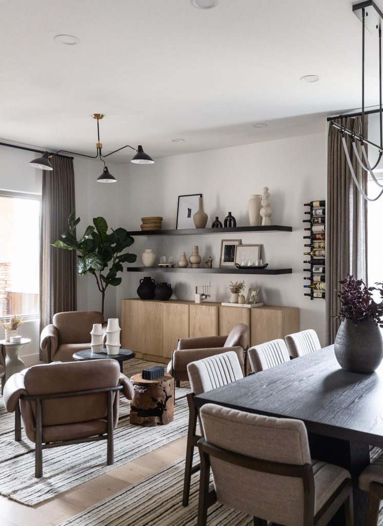 Neutral-toned living and dining area with wooden furniture, potted plants, shelves with ceramics, and large windows with beige curtains. — Living with Lolo.