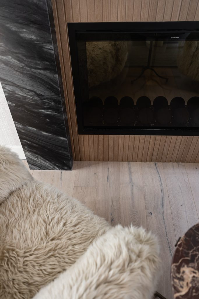 Light wooden flooring, a glass-front modern fireplace, and a beige faux fur chair in an interior space — Living with Lolo.