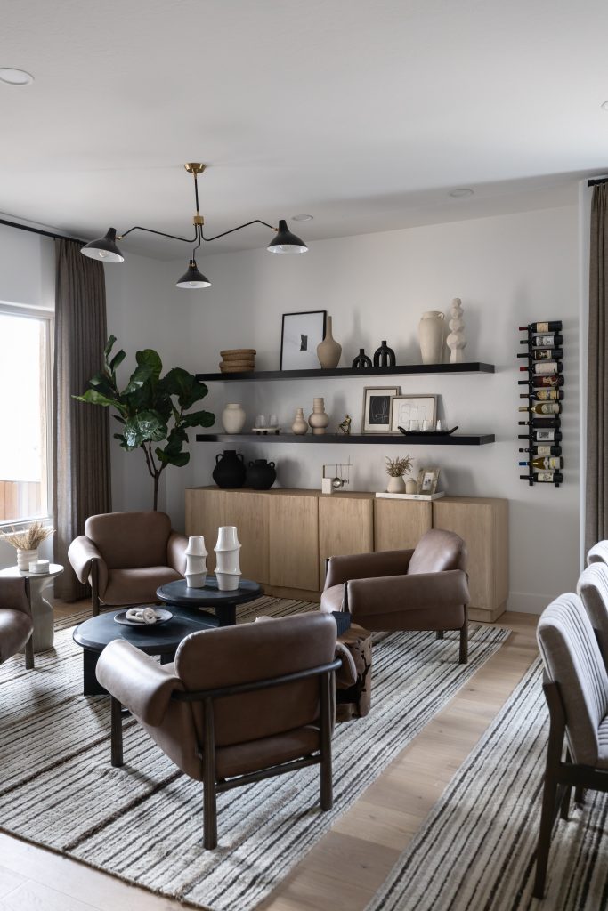 A modern living room with brown leather chairs, a black round coffee table, striped rug, wall shelves, and a corner plant. — Living with Lolo.
