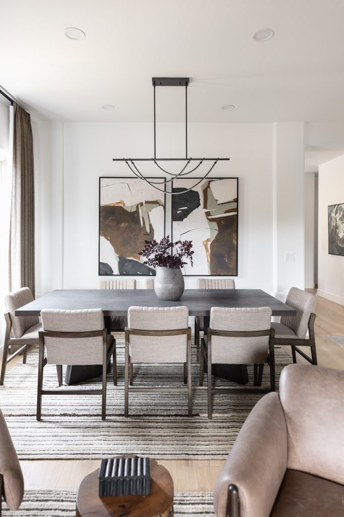 A modern dining room with a dark rectangular table, eight light chairs, a vase of dark foliage, and abstract wall art. — Living with Lolo.