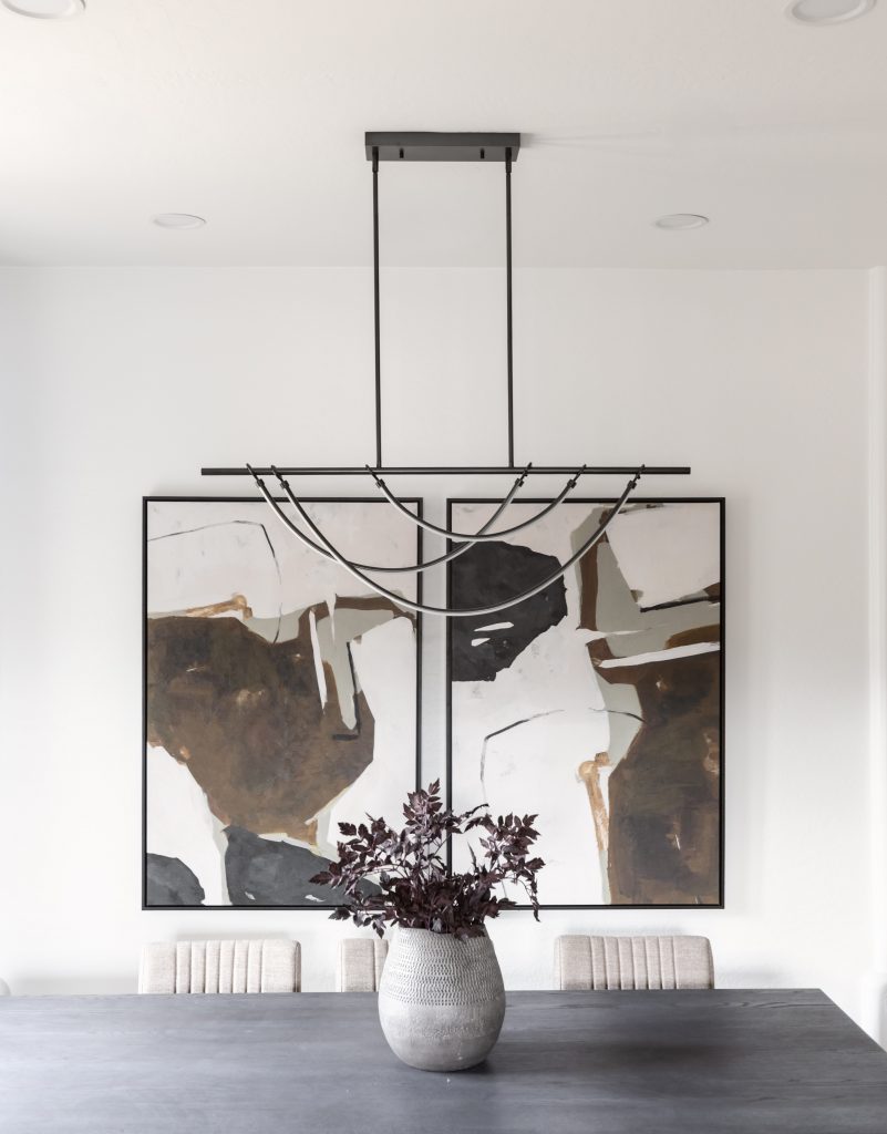 A black dining table with beige chairs, a gray vase with dark leaves, abstract wall art, and a geometric black chandelier.— Living with Lolo.