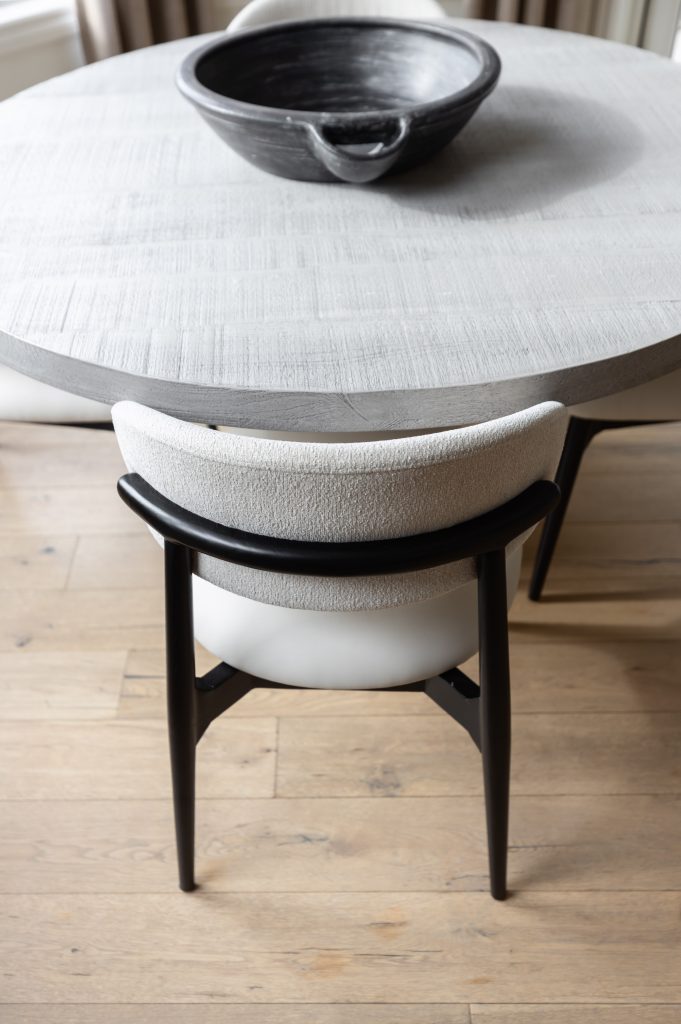A round, light-colored table with a black bowl on top is surrounded by modern chairs on a wooden floor — Living with Lolo.