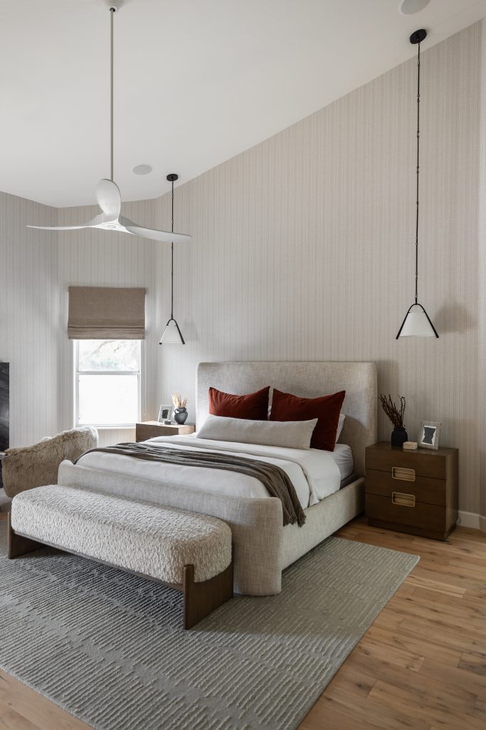 A modern bedroom displays a large upholstered bed, brown accent pillows, bedside tables, pendant lights, and a bench—Living with Lolo.