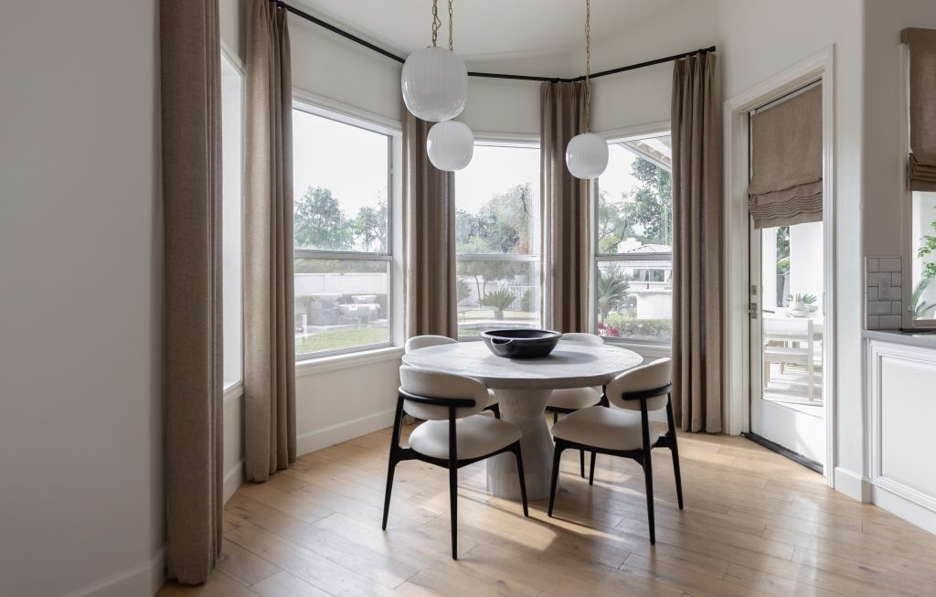 A dining nook with a round table, four chairs, pendant lighting, and large curtained windows overlooking the backyard. — Living with Lolo.