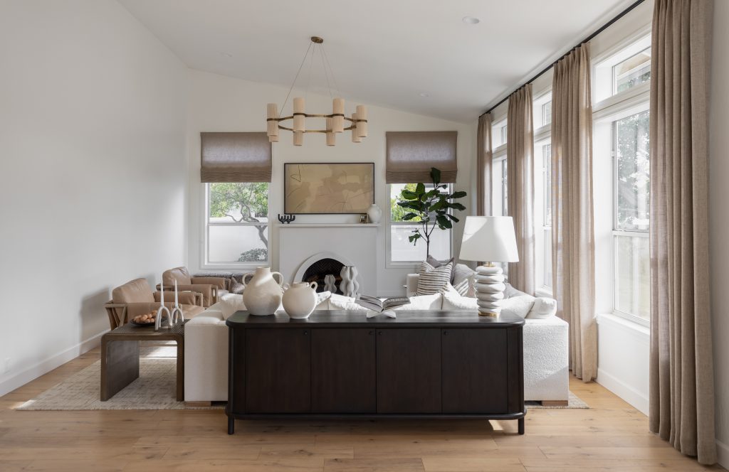 Modern living room with neutral colors, a white sofa, dark console table, armchair, large windows, and beige curtains—Living with Lolo.