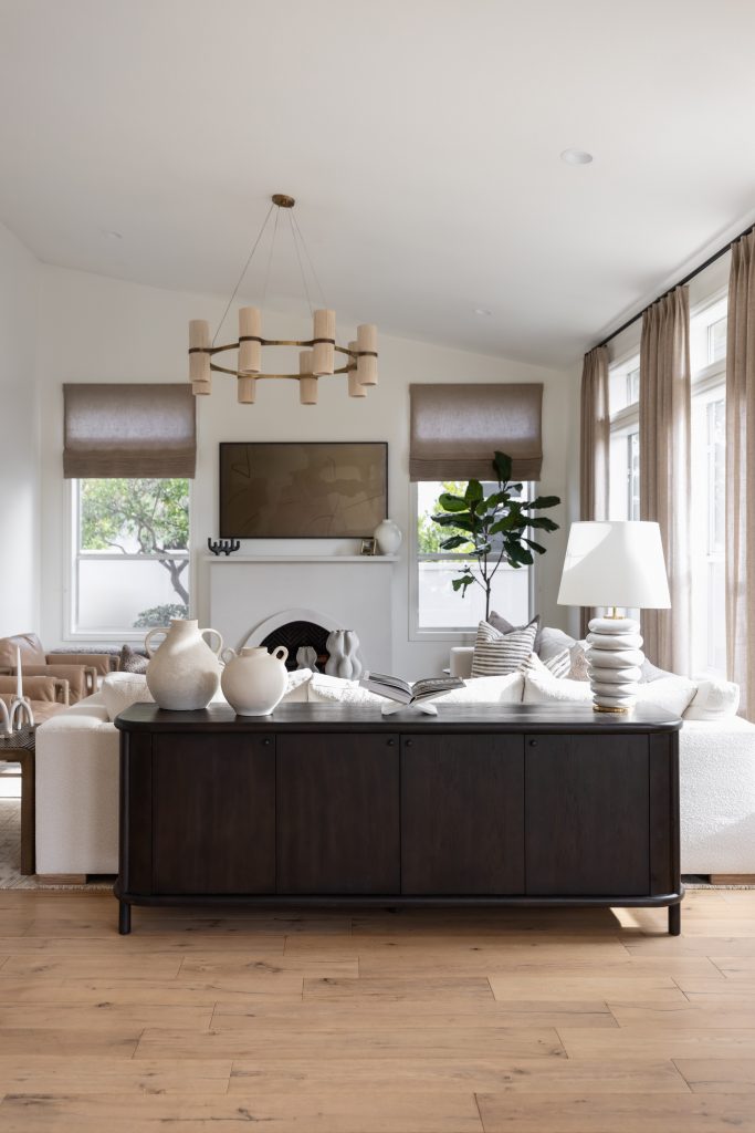 A modern living room with a dark console table, light sofas, round coffee table, fireplace, large curtained windows, and wood floors—Living with Lolo.
