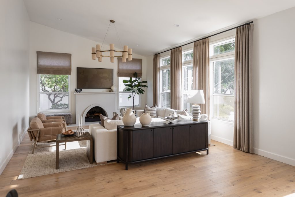 A living room with a beige sectional sofa, light wood floors, large curtained windows, and a wall-mounted TV. — Living with Lolo.