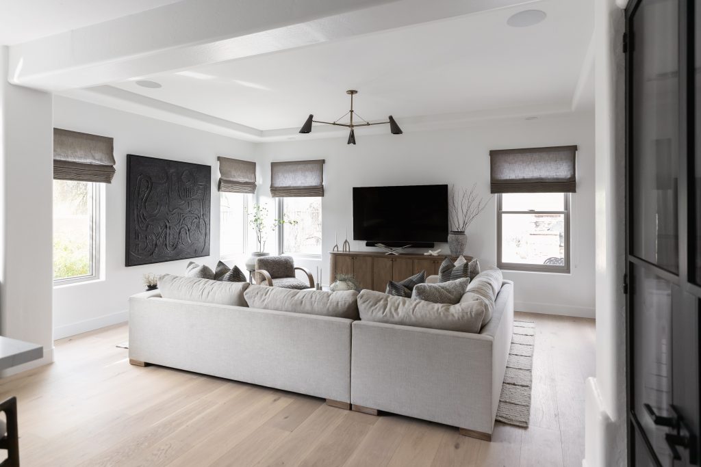 A modern living room with a large sectional sofa, wall-mounted TV, wooden cabinet, abstract wall art, and fabric-shaded windows. — Living with Lolo.