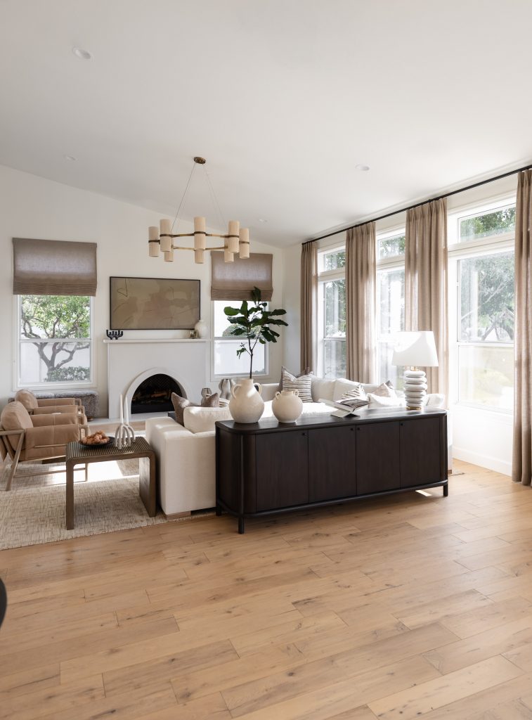 Light wood floors, a white sofa, beige chairs, large curtained windows, a dark sideboard, and a fireplace with art above—Living with Lolo.