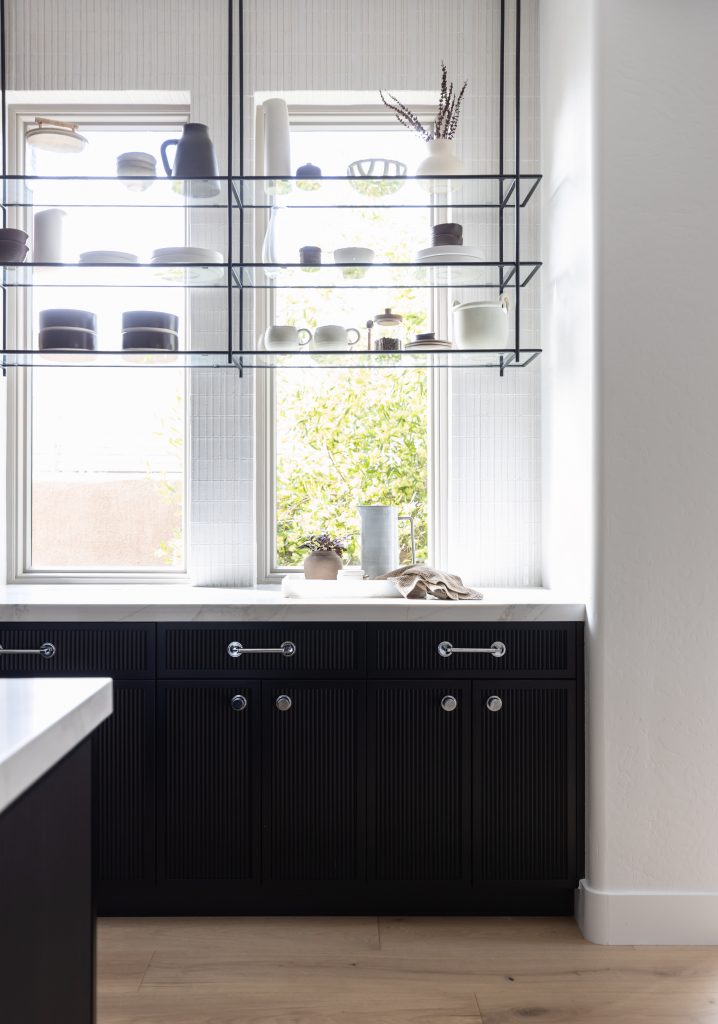 Modern kitchen with dark cabinets, open shelves displaying ceramics, and two large windows providing natural light — Living with Lolo.
