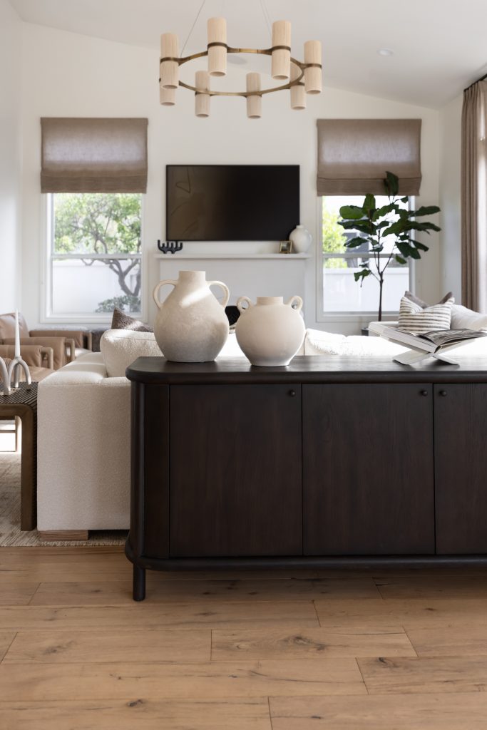 Renovated living room with a dark wood sideboard, two ceramic vases, white sofa, and TV between windows with roman shades. — Living with Lolo.