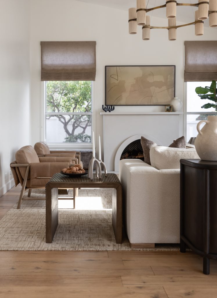 Modern living room with a beige sofa, two tan chairs, wooden coffee table, fireplace, large windows, and minimalist decor— Living with Lolo.