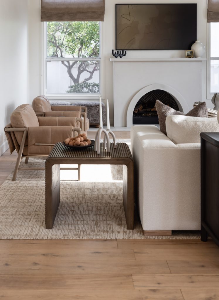 Modern living room with a white sofa, tan armchairs, wooden coffee table, fireplace, large windows, and wall-mounted TV—Living with Lolo.