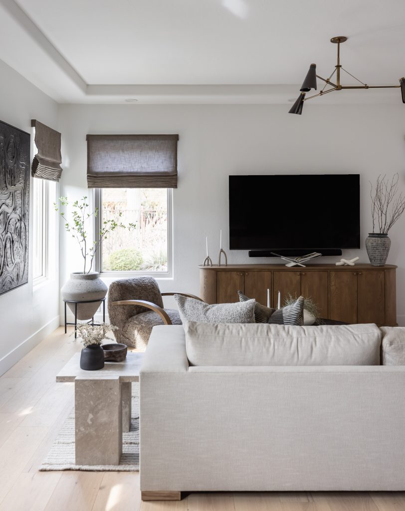 Modern living room featuring a light beige sofa, stone coffee table, wooden sideboard with vases, wall-mounted TV, armchairs, and large window—Living with Lolo.